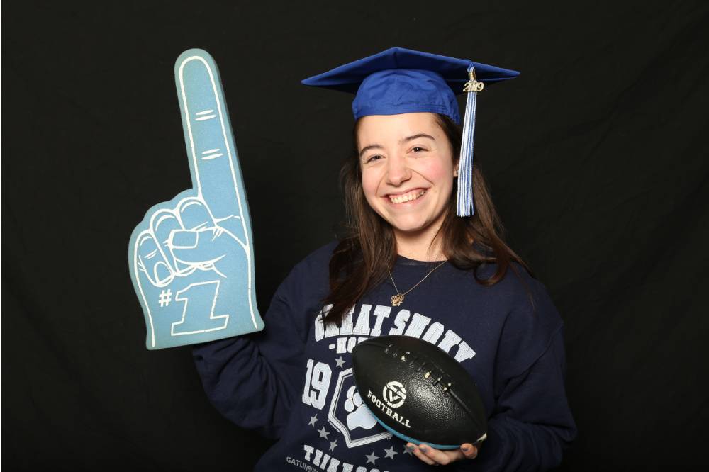 woman in graduation cap with foam finger and football